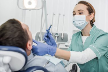 Diş enstrüman tutarak ve diş Kliniği hastada çehresini dokunmadan maskeli kadın diş hekimi
