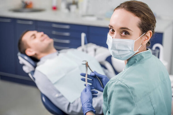 selective focus of female dentist in mask holding dental instrument near patient 