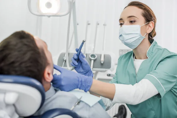 Dentista Feminina Máscara Segurando Instrumento Dentário Tocando Face Paciente Clínica — Fotografia de Stock