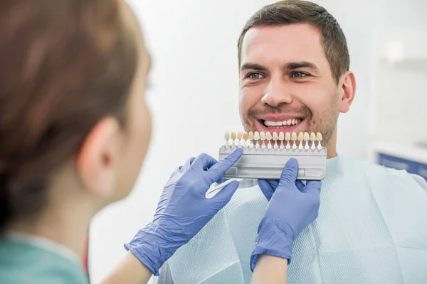 有选择的焦点的人微笑在牙医附近与牙齿调色板在手 — 图库照片