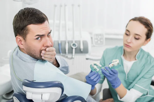 美しい歯科医歯のモデルを保持しての近くに手で口を覆っているハンサムな男の選択と集中 — ストック写真