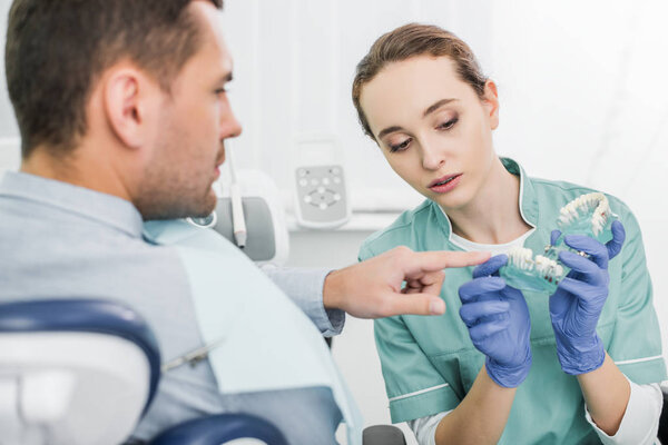 selective focus of man pointing with finger at teeth model near beautiful dentist 