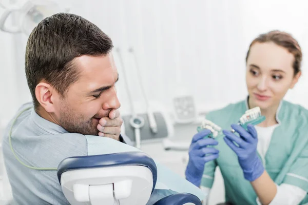 有选择的焦点的人覆盖嘴与手接近美丽的牙医举行牙齿模型 — 图库照片