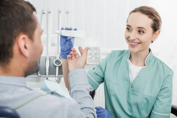 selective focus of attractive dentist holding toothpaste near patient