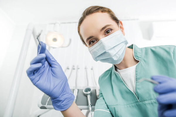 selective focus of female dentist in latex gloves and mask holding dental instruments