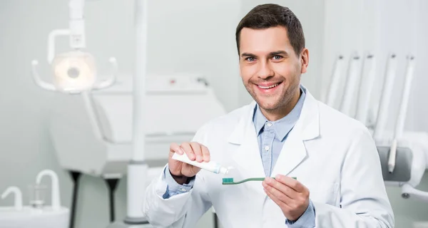 快乐的牙医挤压牙膏在牙刷在牙科诊所 — 图库照片