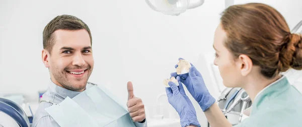 英俊的男人显示拇指附近的女牙医持有牙齿模型的选择性焦点 — 图库照片