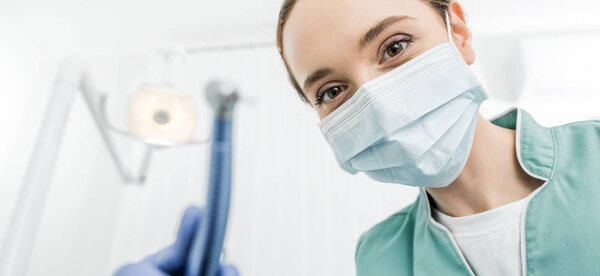 selective focus of female dentist in mask and latex gloves holding dental drill 