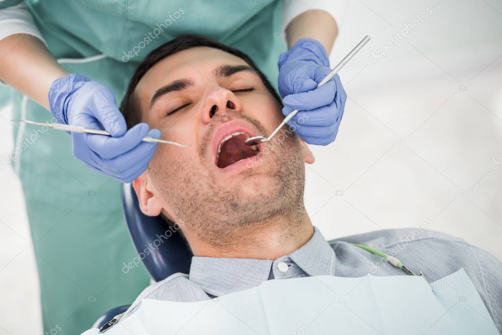 cropped view of female dentist working with patient with opened mouth