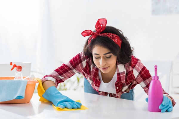 довольно африканская американка в клетчатой рубашке моет стол
