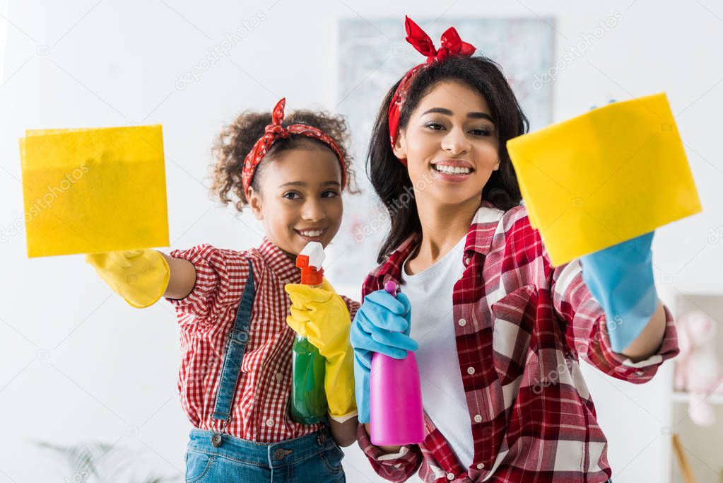 smiling african american mother and dauhgter cleaning house with yellow rags