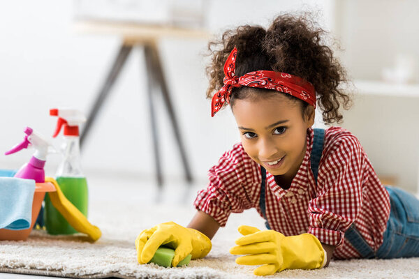 adorable african american child cleaning carpet in yellow rubber gloves