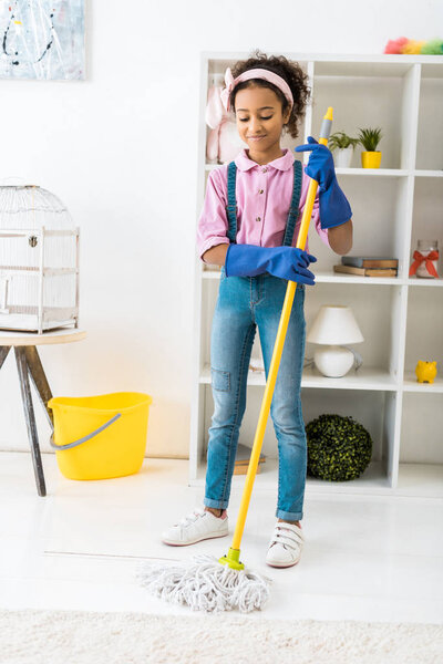 adorable african american girl cleaning floor with mop