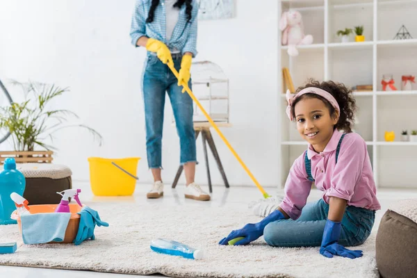 Adorable Africano Americano Niño Limpieza Alfombra Mientras Madre Lavado Piso —  Fotos de Stock