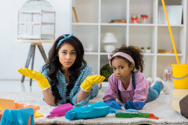 Африканская американская мать и дочь отдыхают на ковре и смотрят в камеру
