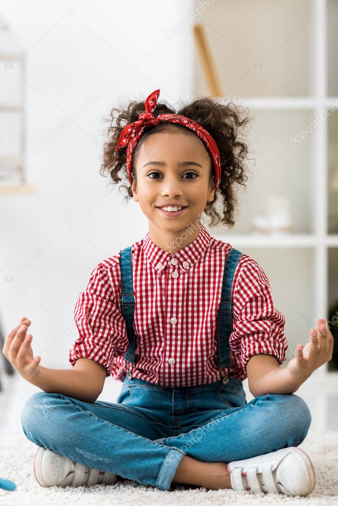 smiling african american child sitting in lotus pose and looking at camera