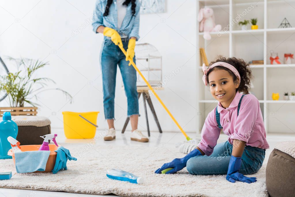 adorable african american child cleaning carpet while mother washing floor with map