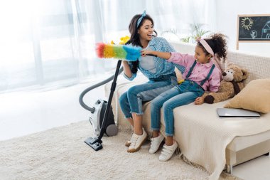 çok güzel Afro-Amerikan çocuk anne ve holding renkli toz bezi gülümseyen kanepede oturan