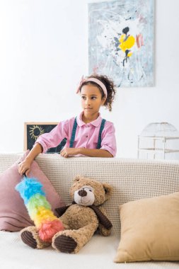 şirin Afro-Amerikan çocuk toz alma kanepe yastık ve oyuncak ayı ile 