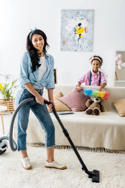 Tersenyum African American Wanita Karpet Dengan Vacuum Cleaner Sementara Putri — Stok Foto