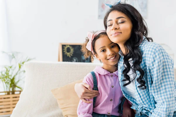 Feliz Africano Americano Mujer Abrazando Adorable Hija Mientras Sentado Sofá —  Fotos de Stock