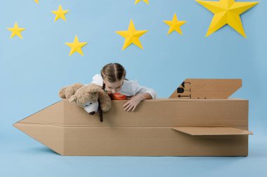 Oyuncak ayı yıldız mavi zemin üzerine karton roket ile oynayan çocuk