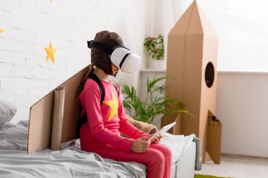 Yatağın üstüne oturan ve dijital tablet kullanarak vr kulaklık evlat