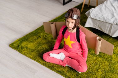 Dalgın uçuş kaskı lotus poz halı üzerinde oturan çocukta