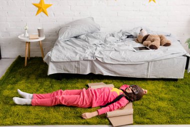 Yorgun çocuk halı yatak odasında yatan karton kanatlı