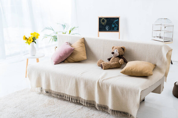 light spacious room with comfortable sofa with pillows and teddy bear 