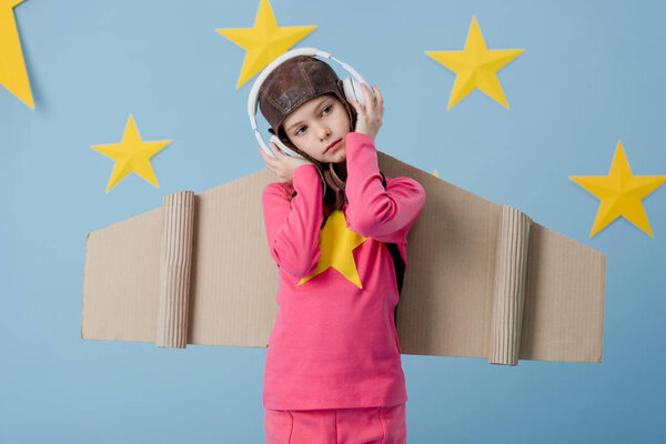 Dreamy child with cardboard wings listening music on blue starry background