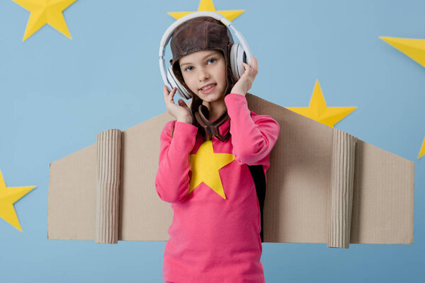 Smiling kid in white headphones looking at camera on blue background with stars
