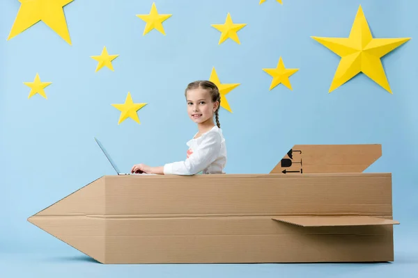 Fröhliches Kind Mit Großer Papprakete Mit Laptop Auf Blauem Sternenhintergrund — Stockfoto