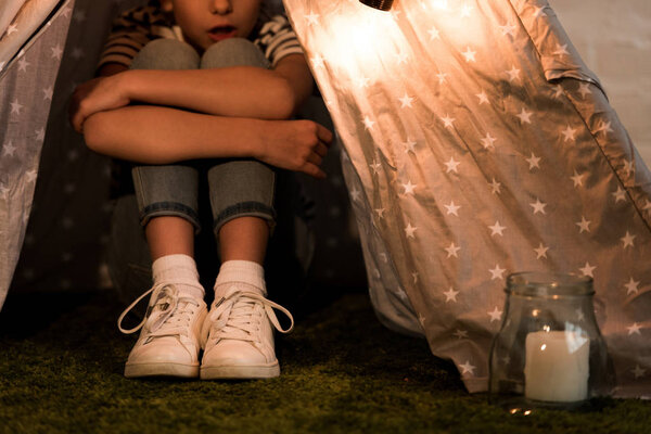 Cropped view of kid sitting in wigwam and embracing knees