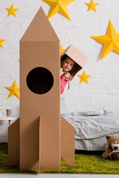 Unbekümmertes Kind Mit Papphelm Steht Hinter Rakete Schlafzimmer — Stockfoto