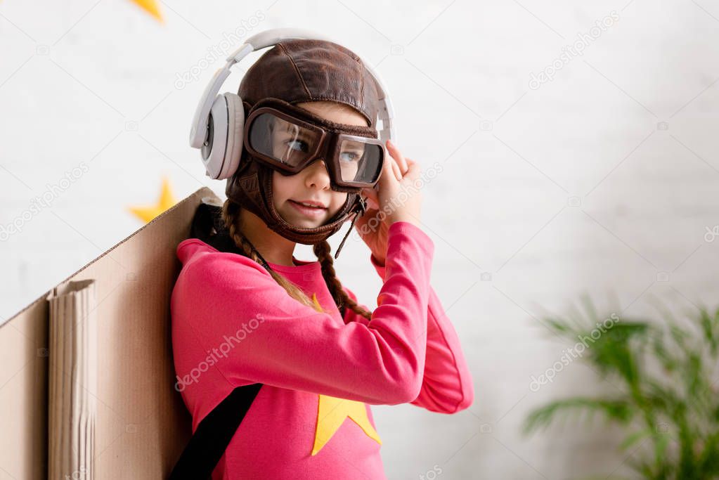 Child in flight helmet and goggles listening music in headphones