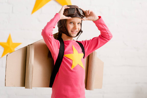 Pleased child with cardboard wings touching goggles with smile