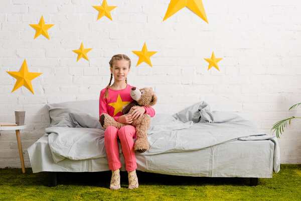 Laughing kid sitting on bed with teddy bear