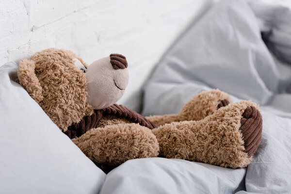 Brown teddy bear lying on grey blanket in room