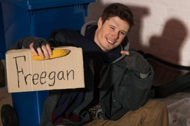 smiling homeless man holding corn cob and holding cardboard card with 