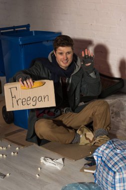 smiling homeless man waving hand while holding cardboard card with 