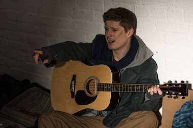 evsiz adam oyun gitar ve şarkı beyaz tuğla duvar dibinde otururken