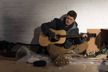 evsiz adam çöp dökümü üzerinde oturan ve gitar çalmak 