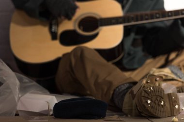 seçici odak evsiz adamın çöp dökümü üzerinde otururken gitar çalmak