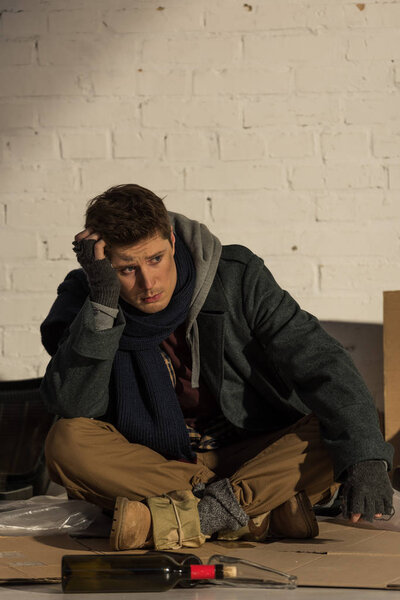 depressed homeless man sitting on cardboard and propping head with hand