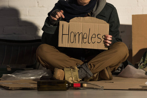 обрезанный вид бездомного, держащего кусок картона с надписью "Бездомный" от руки
