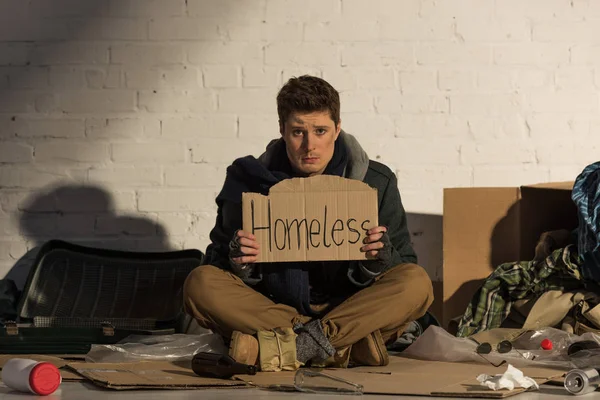 无家可归的痛苦的人拿着纸板卡与 无家可归 手写的文本 而坐在垃圾场 — 图库照片