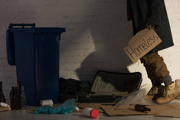 partial view of homeless man holding piece of cardboard with "homeless" handwritten text