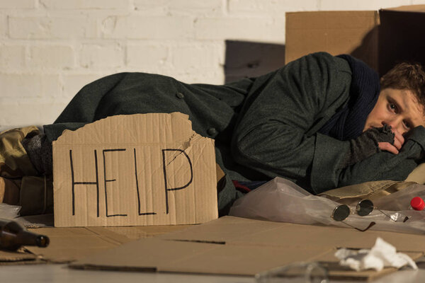 homeless poor man lying on cardboard by white brick wall