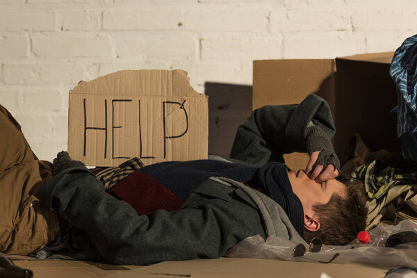 бездомный несчастный лежит на картонке, с надписью "помощь" на карточке
